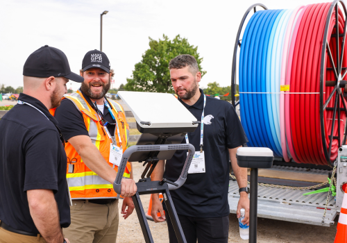 Three guys talking by a machine with red, white and blue wiring behind