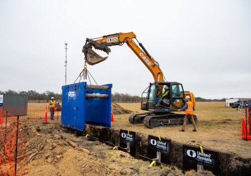 Excavator hoisting trench box into trench on construction site 