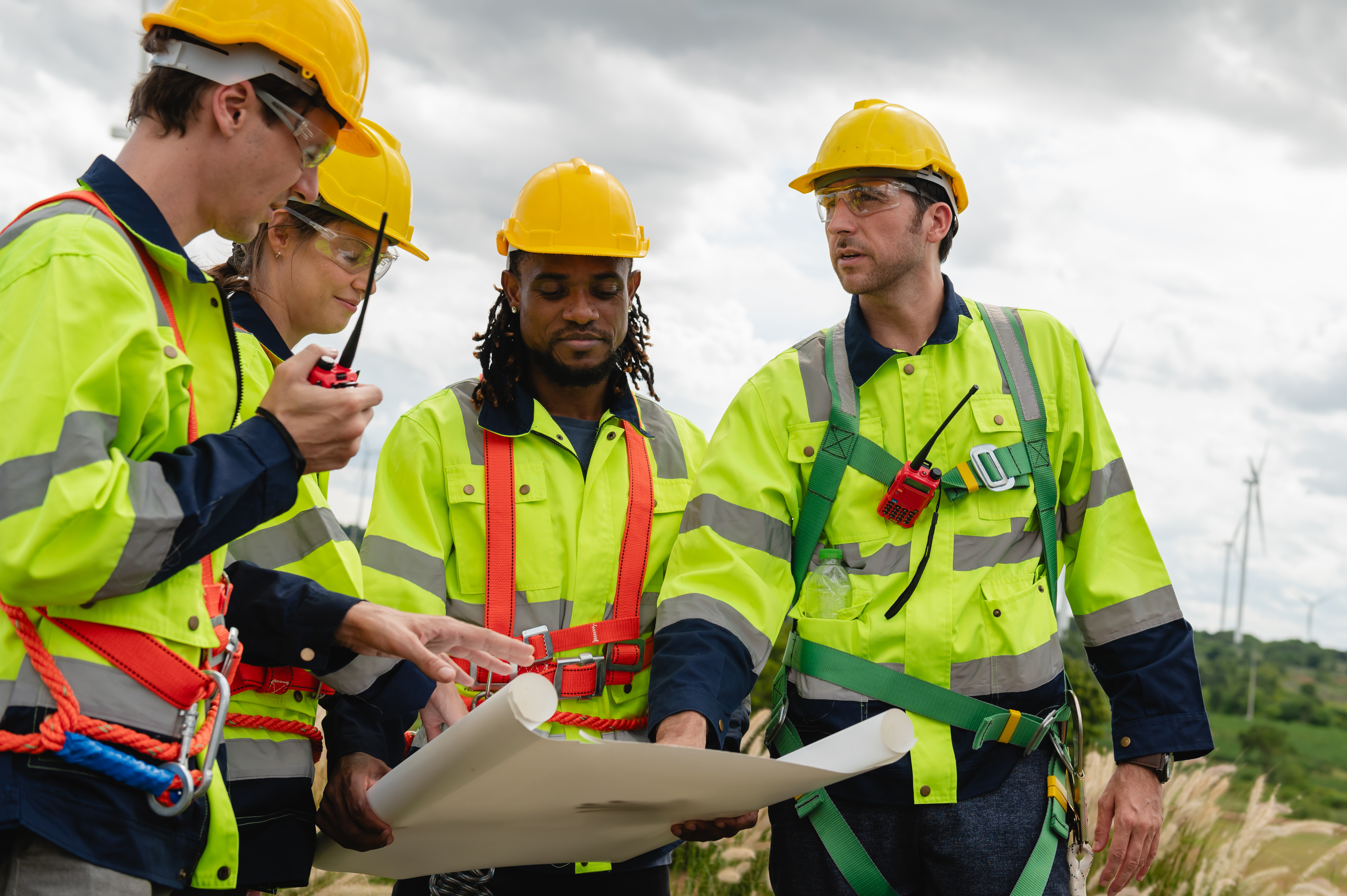 group of construction workers wearing yellow vests and hard hats are looking at a blueprint. They are discussing the details of the project and making sure everything is in order