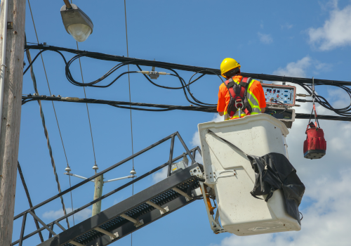 Utility worker wearing safety gear repairs power lines from a bucket lift under a clear blue sky. Perfect for energy, infrastructure, and safety-related visuals.