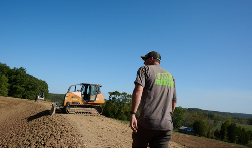 a worker walking on dirt with equipment in the background