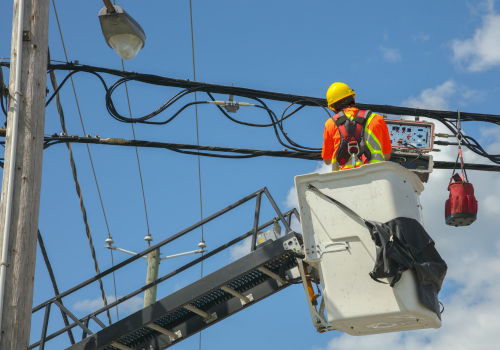 Utility worker wearing safety gear repairs power lines from a bucket lift under a clear blue sky. 