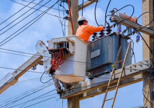 Electrician in bucket of articulated boom lift is repairing electrical transmission on power poles against blue sky background