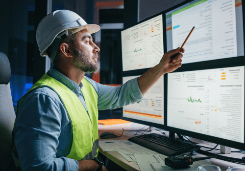 Worker engineer control process of production uses computer with modern SCADA system which showing AI and machine learning. Bearded operator follow of industry process on factory