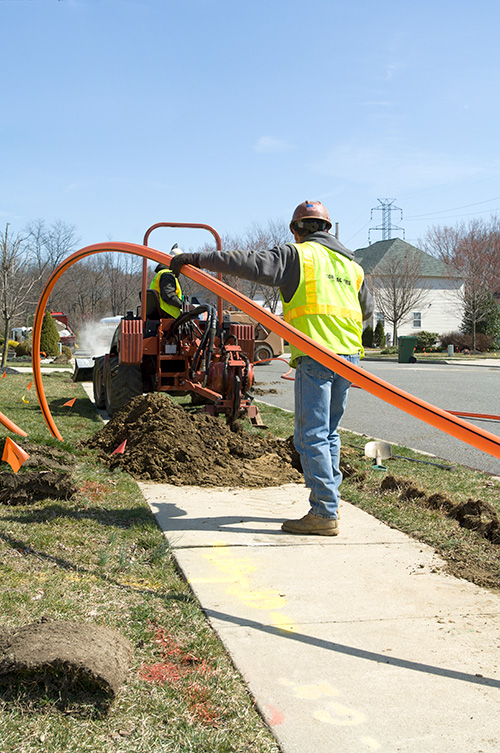 Two installers work together to install conduit for fiber optic cable.