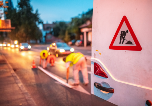 Construction team van with back doors open with a men at work and a Three members of a road maintenance crew getting ready for work. Wearing reflective vests standing next to a van parked on the street.