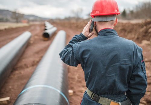 An engineer in a uniform and with a helmet on his head uses a mobile phone while controlling the operation of the gas pipeline