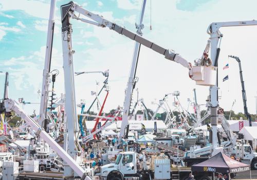 Photo of lots of aerial lift bucket trucks, man in bucket demonstrating lift