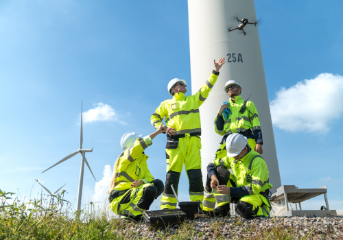 Team of engineers in uniform with helmet safety using drone for inspection and maintenance of wind turbine blade at wind farms or construction site to generate electrical energy, Renewable energy.
