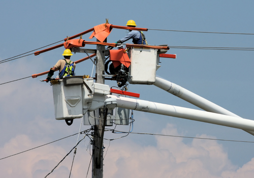 Two hydro workers work high up in boom buckets to repair a defective power line safety