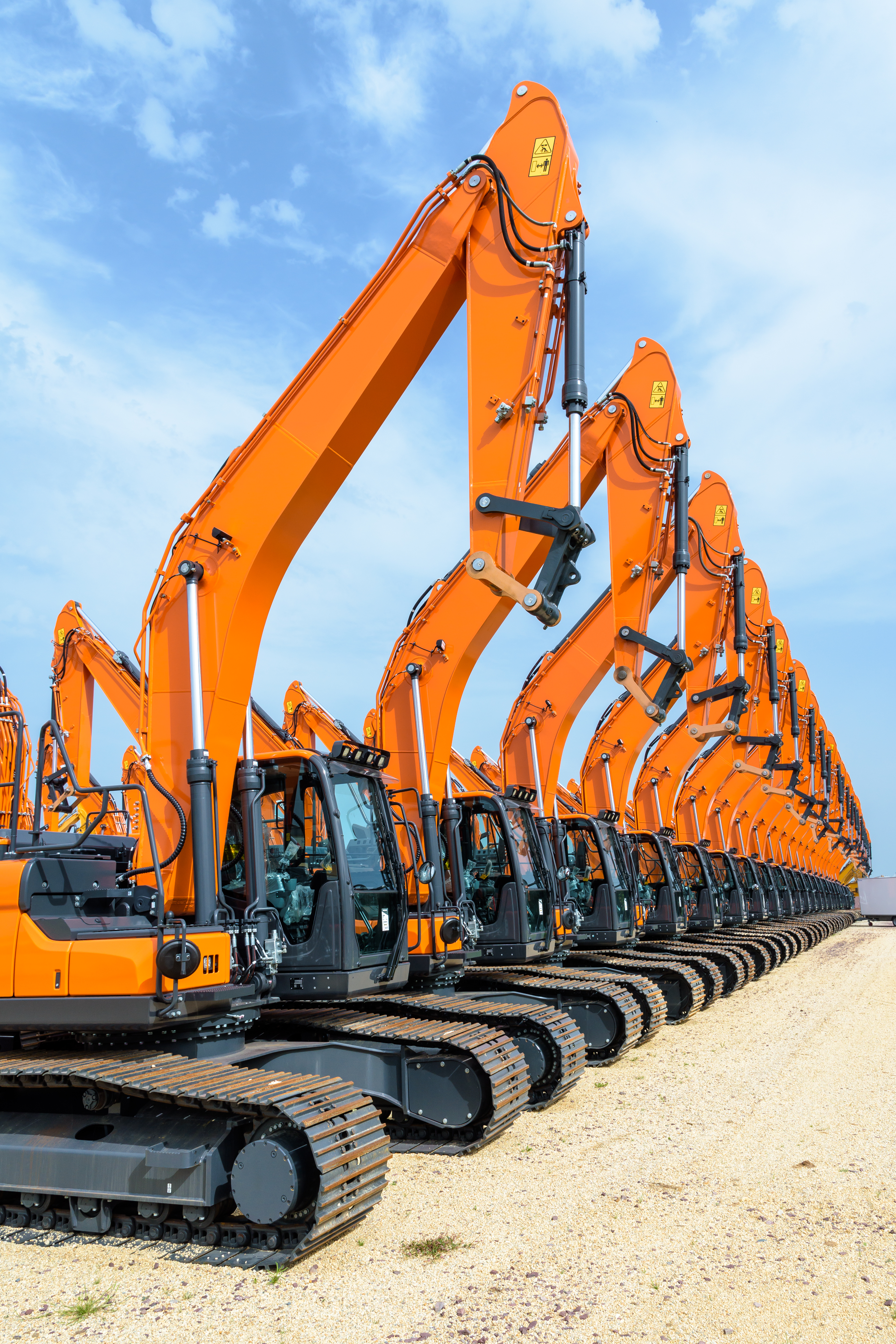 Tens of brand new orange excavators lined up in a row outdoors under a stormy sky.